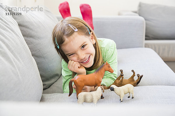 Porträt des lächelnden Mädchens auf der Couch mit ihren Tierfiguren