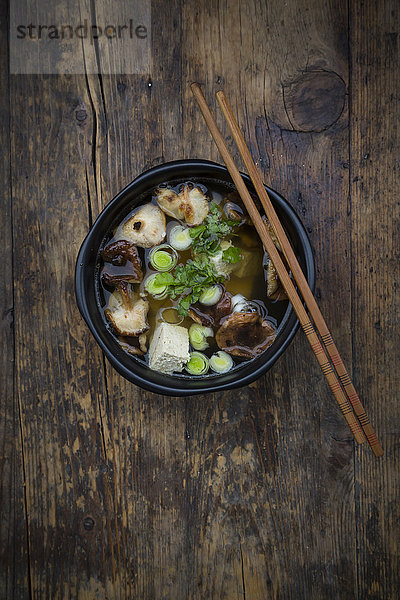Schüssel Misosuppe mit Bio-Tofu  Shitake-Pilzen  Lauch und Petersilie auf dunklem Holz