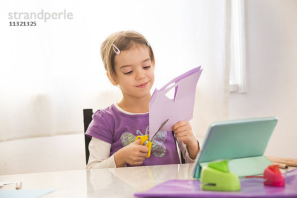 Kleines Mädchen  das zu Hause klimpert  schneidet Papier mit Online-Hinweisen.