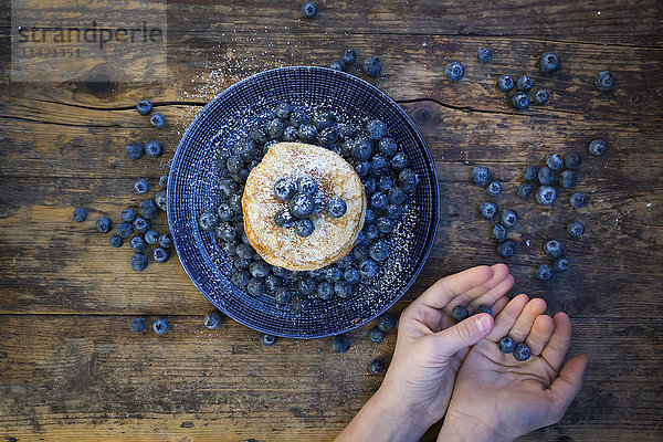 Pfannkuchen mit Blaubeeren auf Teller und Mädchenhänden