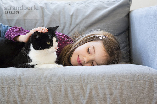 Kleines Mädchen auf der Couch liegend  Katze streichelnd