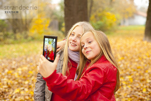 Zwei glückliche Mädchen nehmen Selfie mit Handy im Herbst