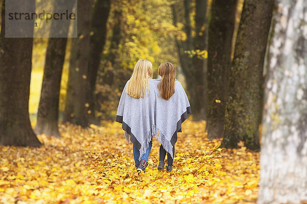 Rückansicht von zwei Mädchen  die sich im Herbst das Cape teilen