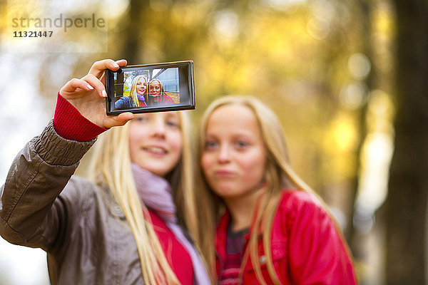 Zwei Mädchen nehmen Selfie mit Handy im Herbst