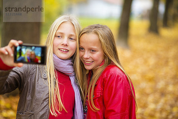 Zwei lächelnde Mädchen nehmen Selfie mit Handy im Herbst