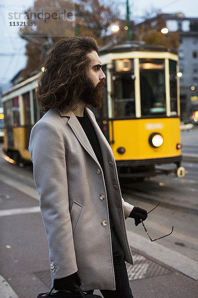 Stilvoller junger Mann steht an der Straßenbahnhaltestelle
