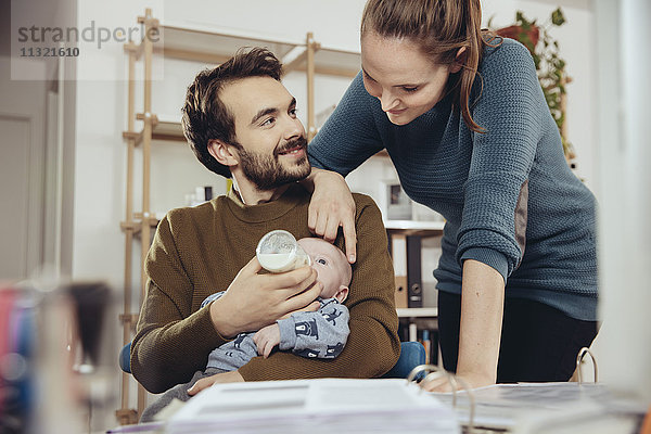 Mutter schaut Vater beim Füttern des Babys im Home-Office an