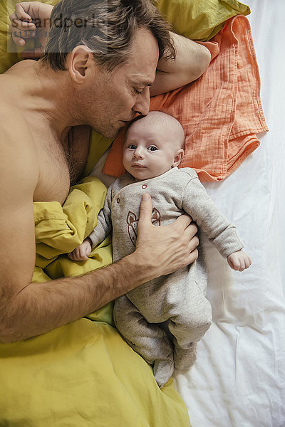 Vater kuschelt im Bett mit seinem neugeborenen Baby