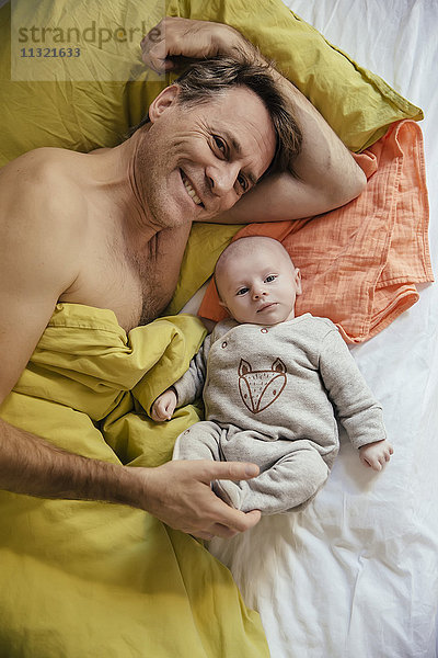 Lächelnder Vater liegt mit seinem neugeborenen Baby im Bett.
