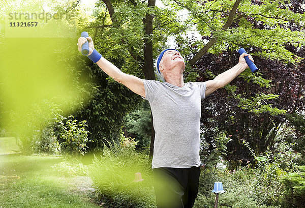 Senior Mann beim Fitnesstraining mit Kurzhanteln im Garten