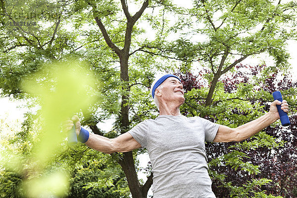 Senior Mann beim Fitnesstraining mit Kurzhanteln im Garten