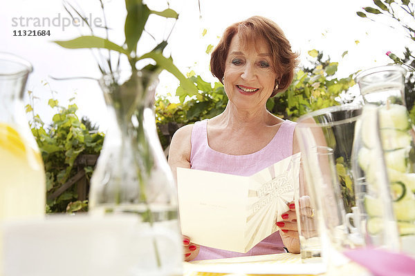 Seniorin im Garten sitzend  mit Geburtstagskarte