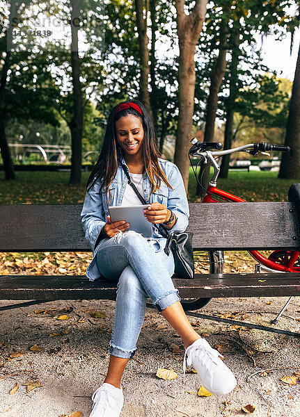 Lächelnde junge Frau sitzt auf einer Bank im Park und hält eine Tafel.