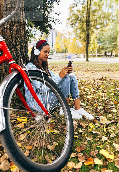 Junge Frau  die im Herbst mit ihrem Smartphone im Park Musik hört.