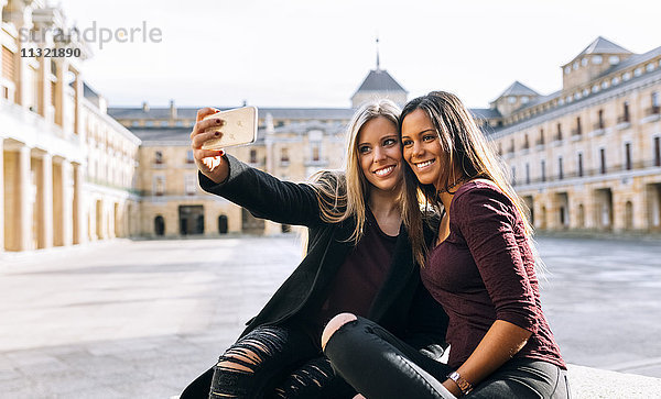Zwei lächelnde junge Frauen auf dem Stadtplatz  die einen Selfie nehmen.