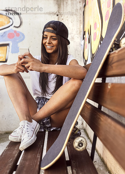 Lächelnde junge Frau mit Skateboard auf dem Handy