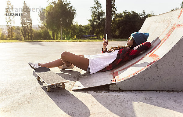 Junge Frau mit Skateboard und Handy im Skatepark