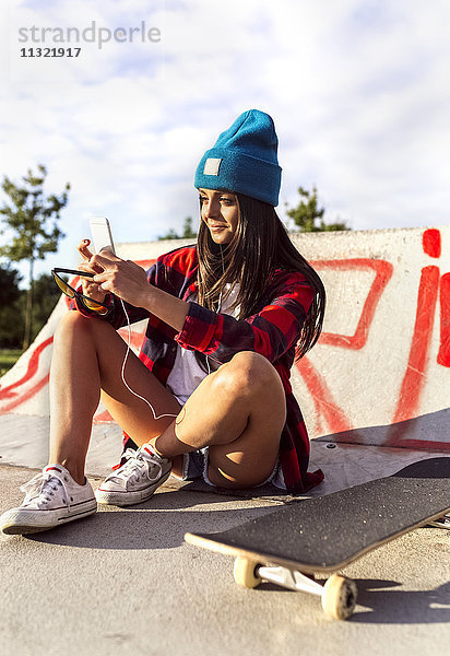 Junge Frau mit Skateboard und Handy im Skatepark