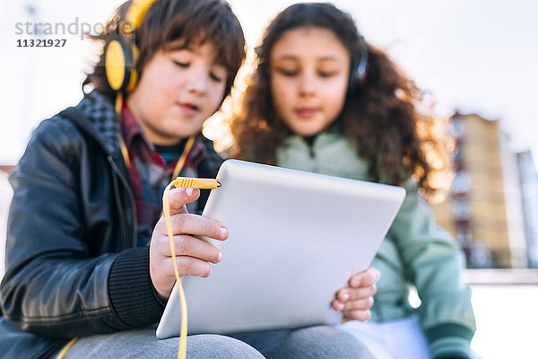 Zwei Kinder beim Musikhören mit Kopfhörer und Tablett