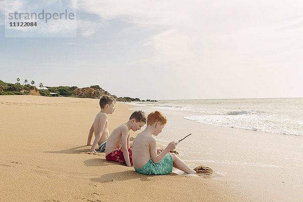Drei Jungen sitzen am Strand.