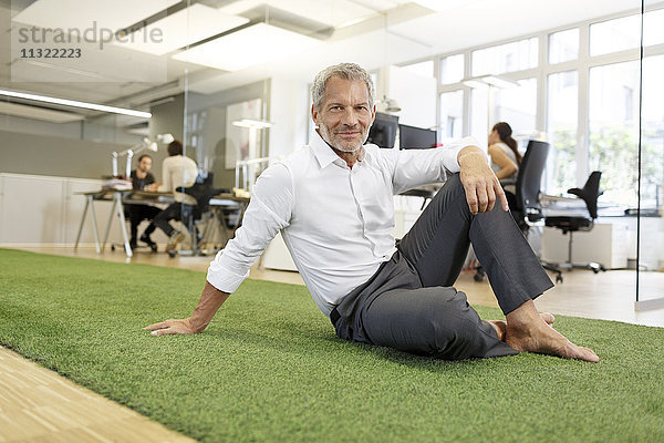 Lächelnder Geschäftsmann sitzt auf Teppich im Büro