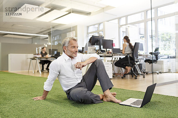 Geschäftsmann sitzt auf Teppich im Büro mit Laptop
