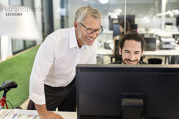 Zwei lächelnde Männer im Büro mit Blick auf den Computerbildschirm