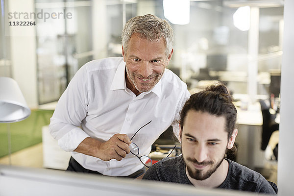 Zwei lächelnde Männer im Büro mit Blick auf den Computerbildschirm