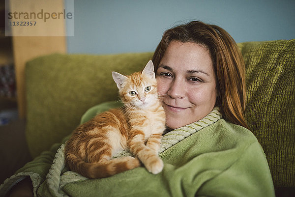 Porträt einer glücklichen Frau mit ihrem Kätzchen auf der Couch zu Hause