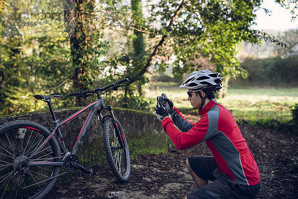 Mountainbiker beim Fotografieren im Wald mit seinem Smartphone