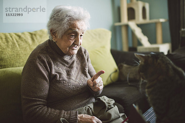 Seniorin sitzt auf der Couch und schimpft mit ihrer Katze.