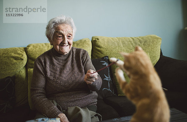 Lächelnde Seniorin beim Spielen mit ihrem Kätzchen zu Hause