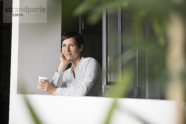Lächelnde Frau mit Tasse Kaffee am Fenster