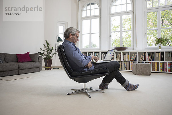 Erwachsener Mann zu Hause sitzend im Stuhl mit Laptop