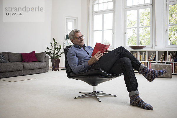 Erwachsener Mann zu Hause sitzend im Stuhl Lesebuch