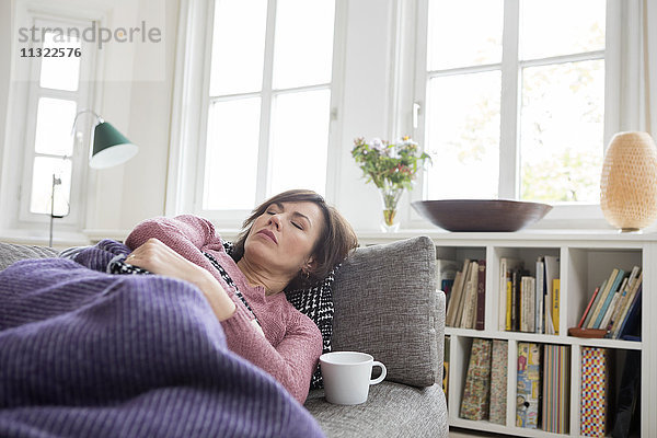 Frau mit Bauchschmerzen auf dem Sofa liegend