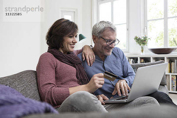Lächelndes reifes Paar zu Hause auf dem Sofa online einkaufen