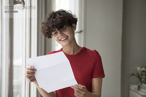 Porträt einer lächelnden jungen Frau beim Lesen eines Briefes