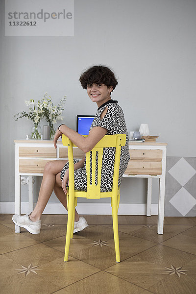 Porträt einer lächelnden jungen Frau  die zu Hause auf einem gelben Stuhl sitzt.