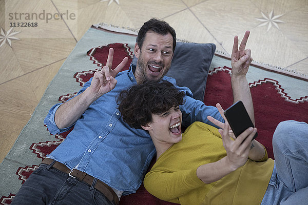 Paar  das zusammen auf dem Teppich liegt und Selfie mit Smartphone nimmt