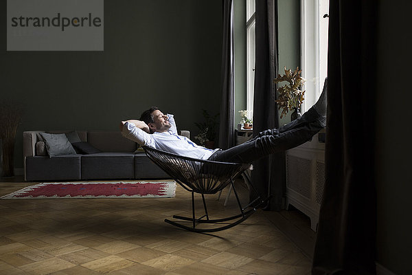 Mann entspannt auf Schaukelstuhl in seinem Wohnzimmer