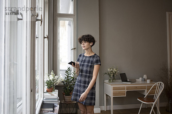 Porträt einer jungen Frau mit Smartphone und Kopfhörer zu Hause