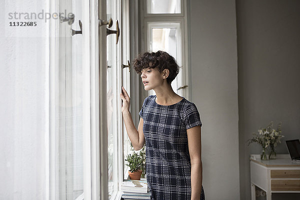 Porträt einer jungen Frau  die zu Hause durchs Fenster schaut.