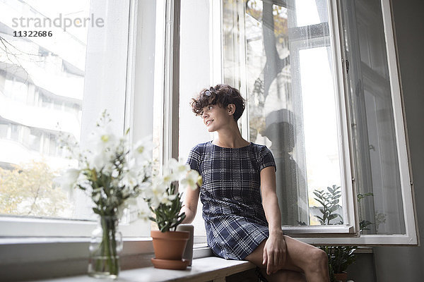 Junge Frau auf der Fensterbank zu Hause sitzend