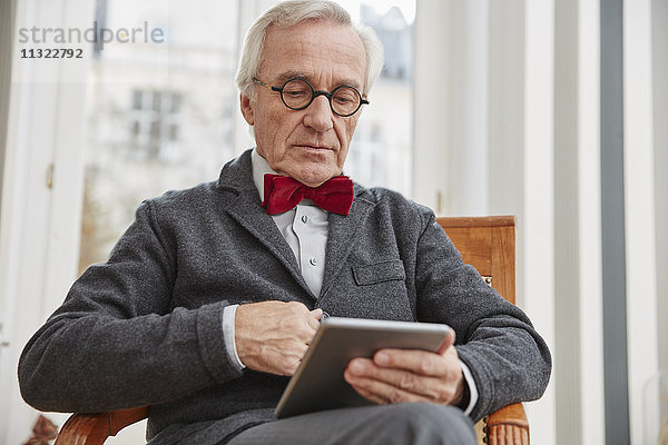 Älterer Mann auf Stuhl sitzend mit Tablette
