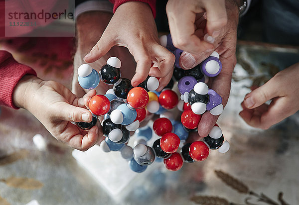 Hände von Großvater und Enkelkindern beim Zusammenbau des molekularen Modells