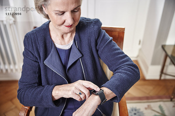 Seniorin auf Stuhl sitzend mit Blick auf smartwatch