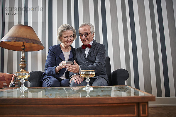 Glückliches Seniorenpaar sitzt auf der Couch mit Smartphone