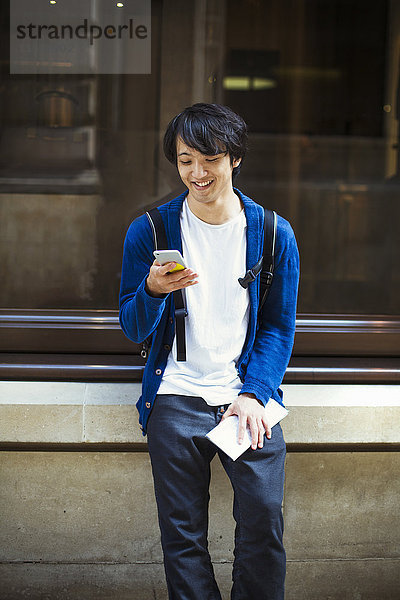 Junger Japaner genießt einen Tag in London mit einem Smartphone.