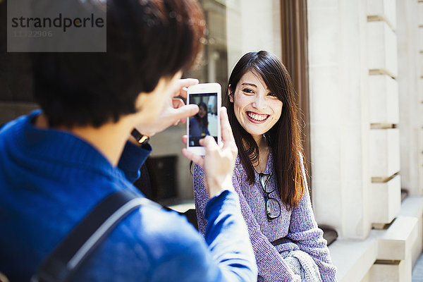 Ein junger Japaner und eine junge Japanerin genießen einen Tag in London  stehen auf einem Bürgersteig und machen ein Foto.